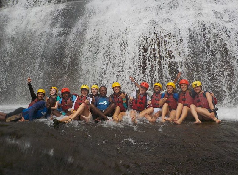 Teens sitting under a waterfall in Fiji on marine biology shark camp