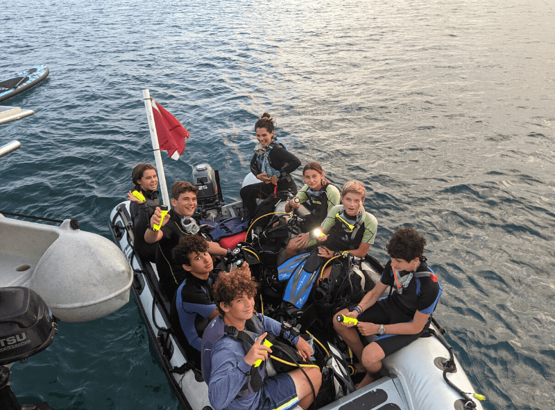 Teens in dive gear in dinghy at advanced dive camp