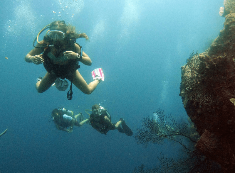 Teens scuba dive next to coral on advanced dive trip