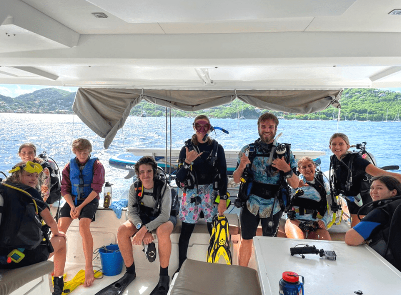 Group of teens in dive gear on catamaran for windward islands advanced scuba trip