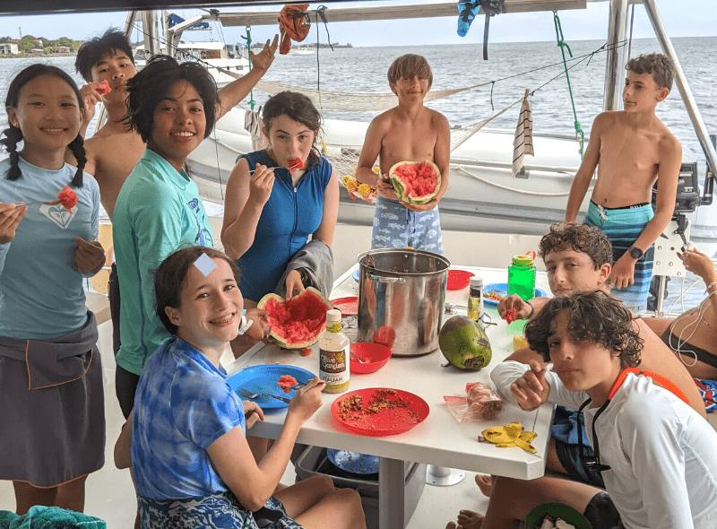 Group of middle school students eat watermelon on catamaran during summer dive and sail camp