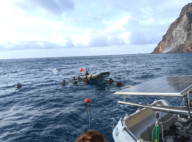 Teens in dive gear in water around dinghy at advanced scuba camp