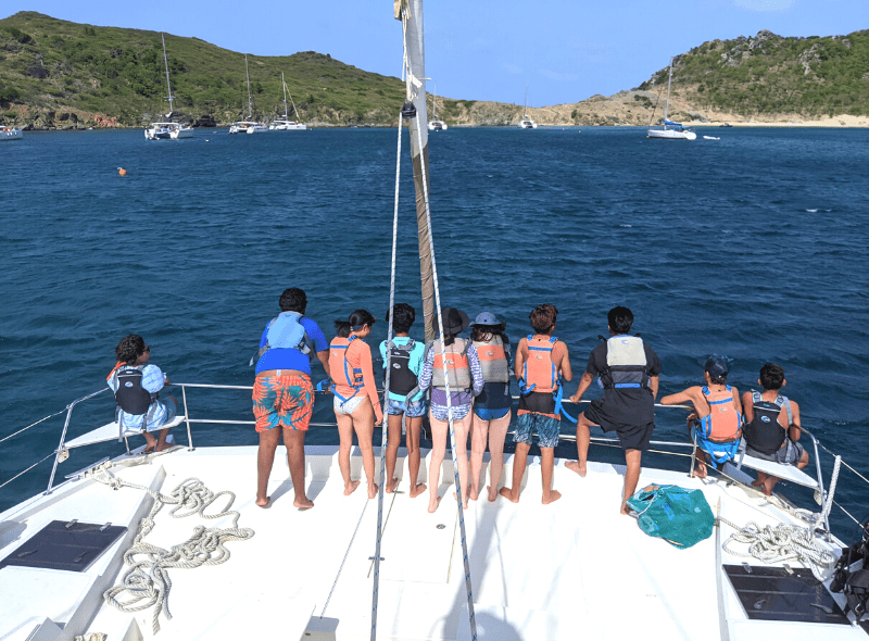 Group of teens at bow of catamaran with Caribbean island in background at summer camp