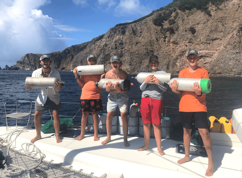 Middle school students hold air tanks on catamaran on advanced dive trip