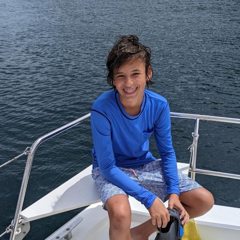 Middle school boy holds snorkel gear on boat in Caribbean during summer sailing program