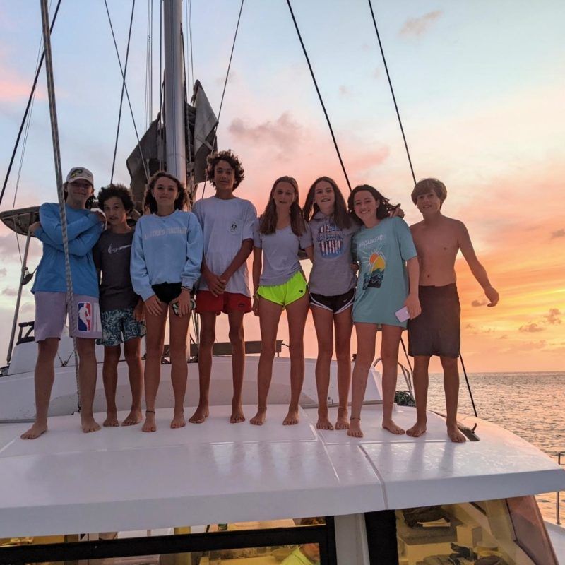 group of middle school students on catamaran pose together at sailing camp