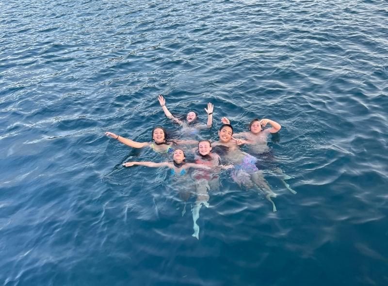 Group of middle school boys and girls swim in water on summer dive and sail trip