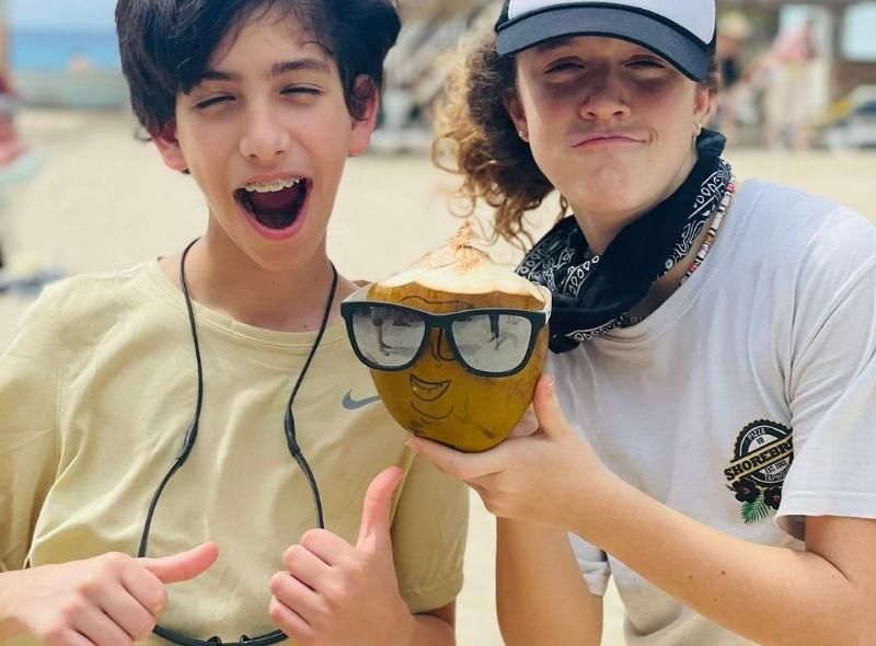 Two middle school students on beach with a coconut participate in middle school sailing camp abroad