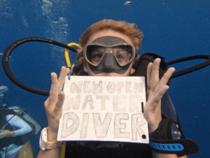 teen diver holds sign that says "new open water diver" after earning scuba certification on a Broadreach trip