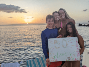 Four Broadreach students hold Master Diver sign at sunset on boat in Caribbean