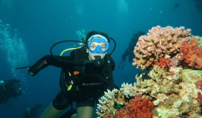 High school student dives with vibrant coral in Red Sea on advanced dive summer program for teens