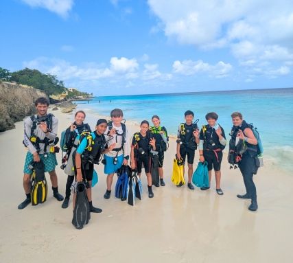 middle school students stand on Bonaire beach in scuba gear on marine biology program