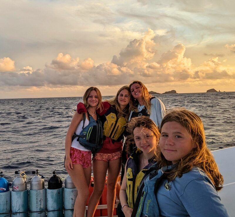middle school students pose on catamaran at sunset