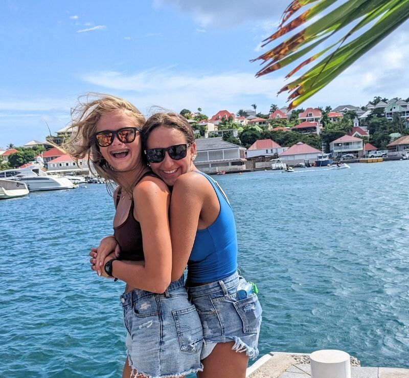 two middle school girls embrace with Caribbean town in background