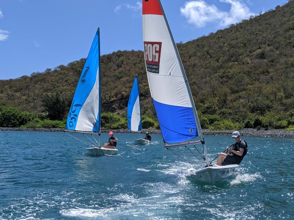 three high school students sail three dinghy sailboats in the Caribbean