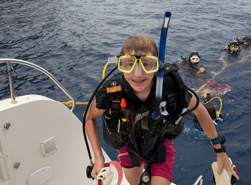 middle school student in scuba gear emerges from water onto catamaran in the Caribbean at scuba camp