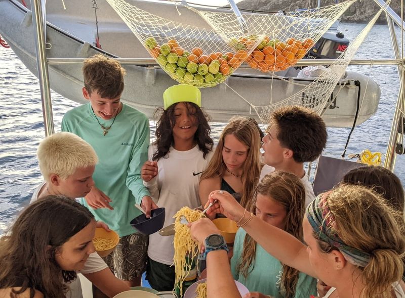 group of middle school students gather eating dinner together on catamaran during summer scuba and sailing camp