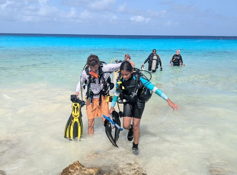 group of middle school students in scuba gear emerge from water onto Bonaire beach on marine biology and scuba camp