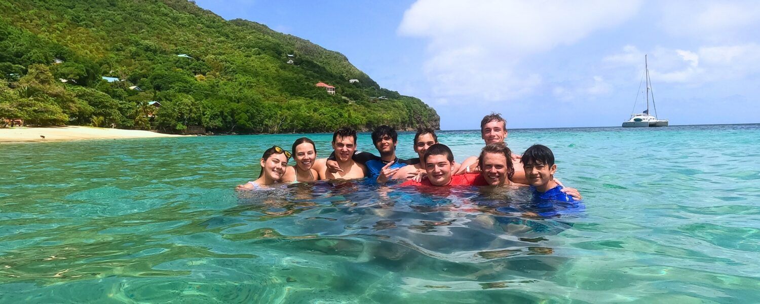 Group of teens swimming together in clear turquoise water near a beach in Bequia in the Caribbean