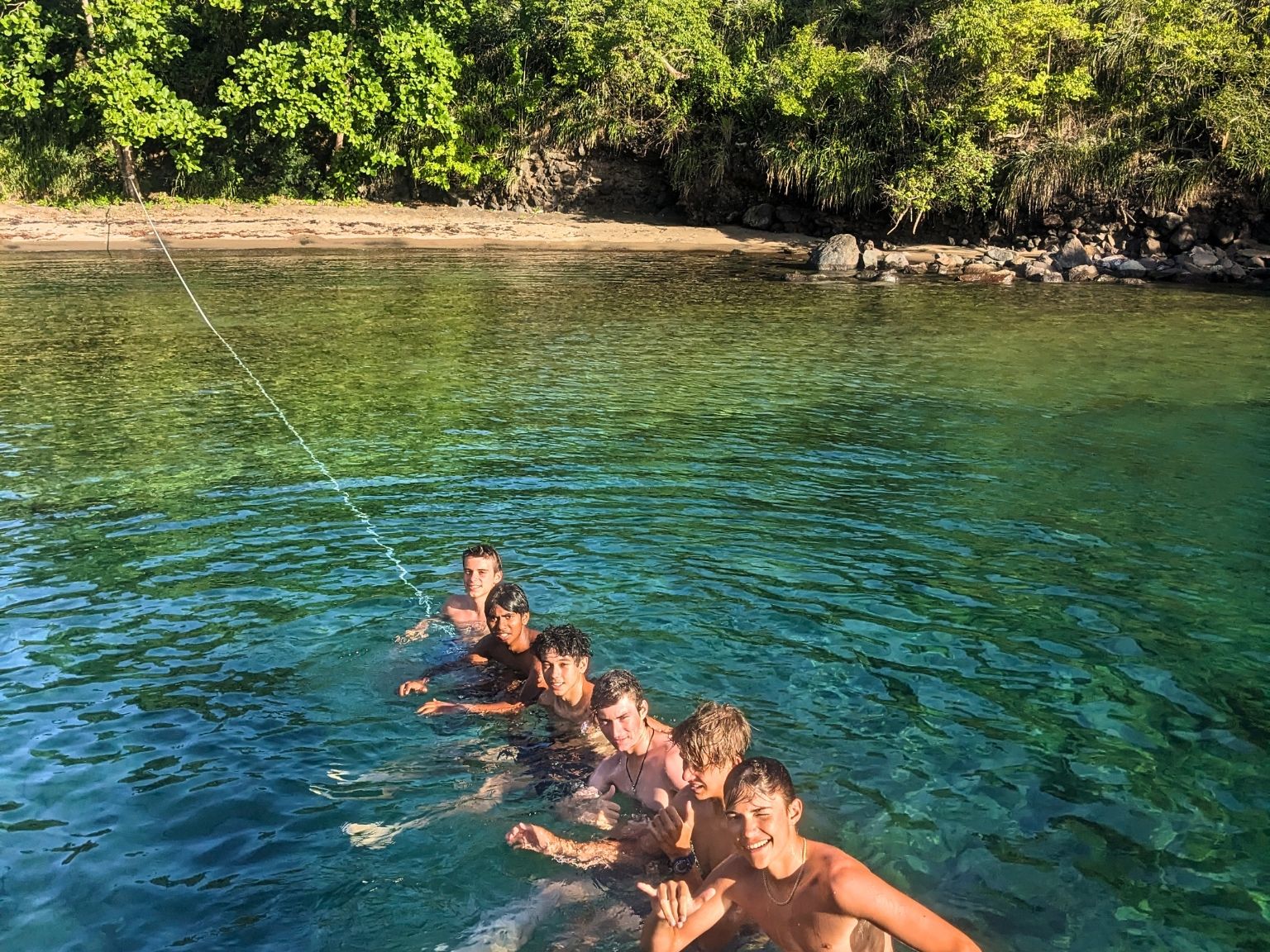 Group of teens floating in the ocean holding a rope near a tropical shoreline