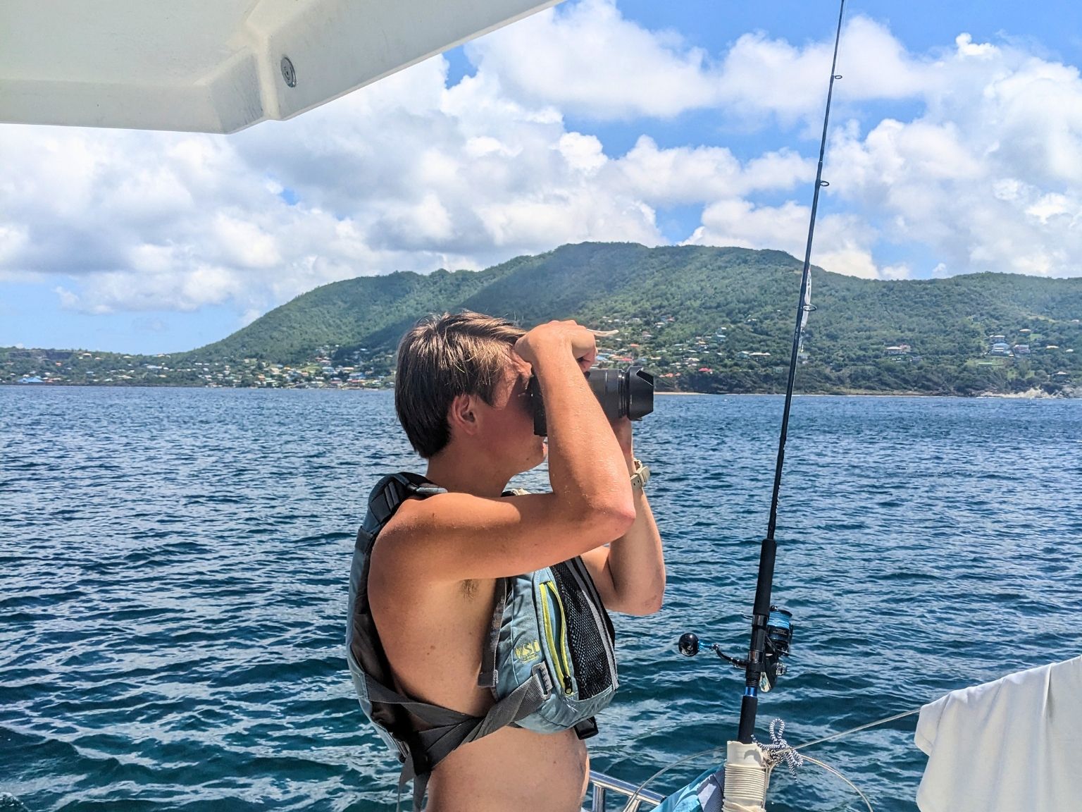 Teen student using binoculars on a sailboat while fishing in the Caribbean Sea
