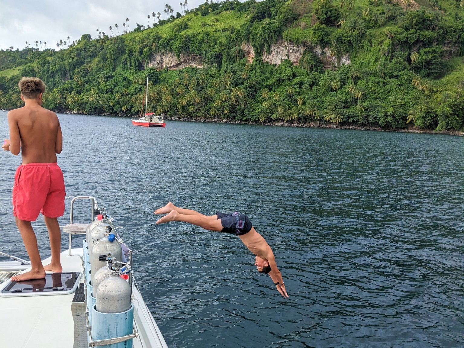 Teen student diving off a catamaran into deep blue water with lush volcanic cliffs in St. Vincent
